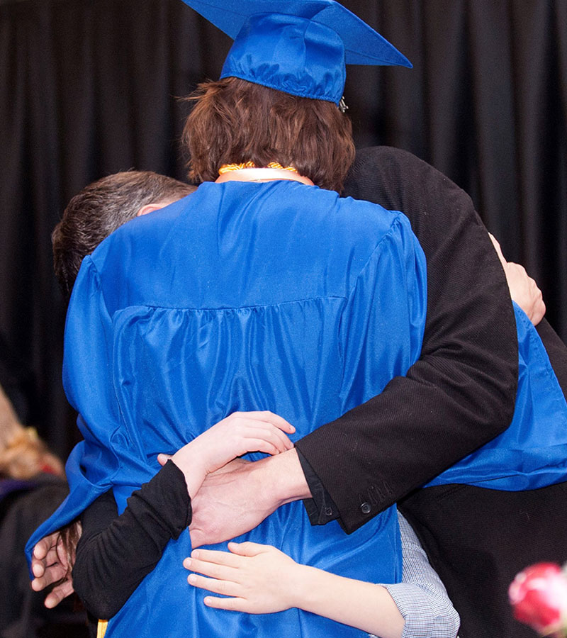 photo - parents surround and hug their graduating daughter
