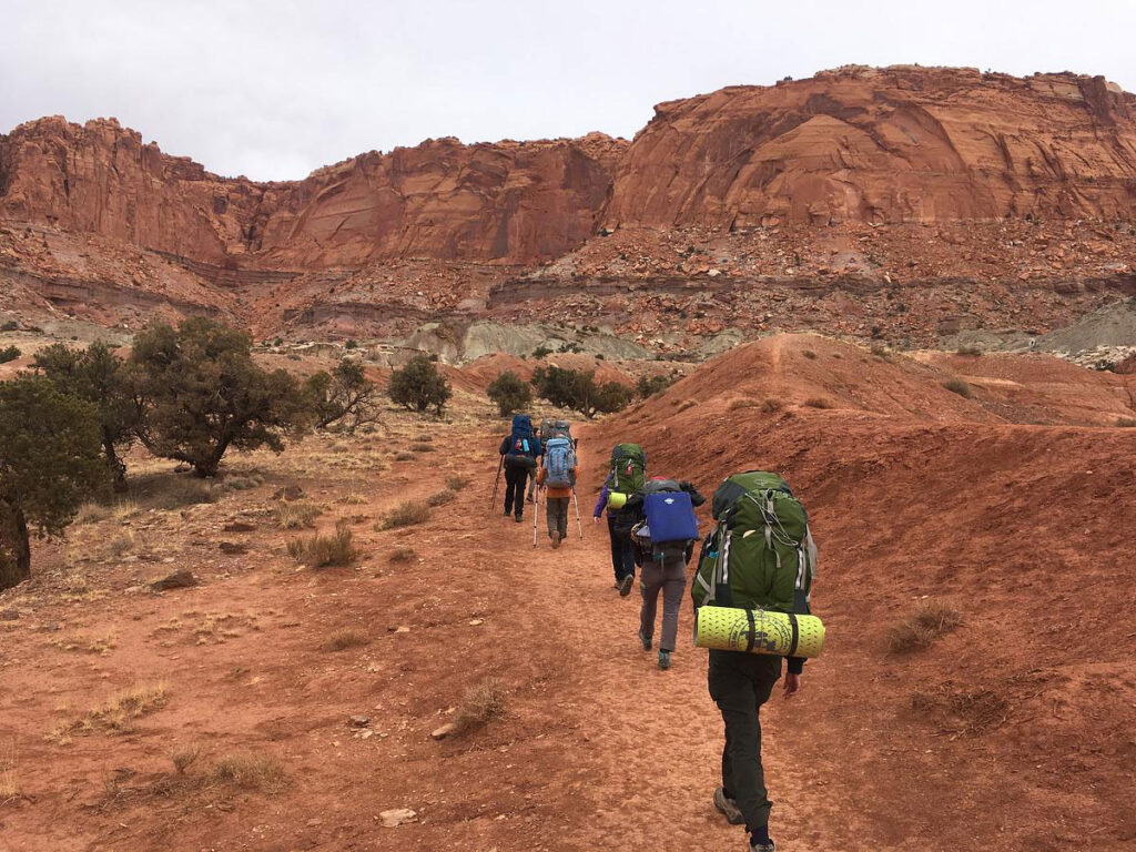 CMC Outdoor Education students hike into the Capitol Reef National Park with backpacks.