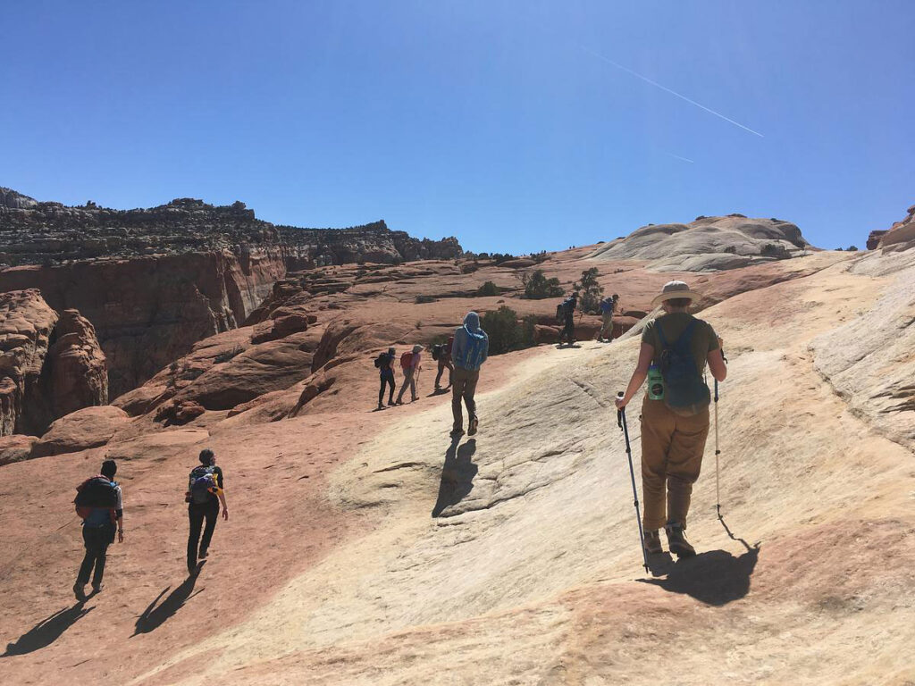 CMC Outdoor Education students hike over slick rock during a desert orientation trip.
